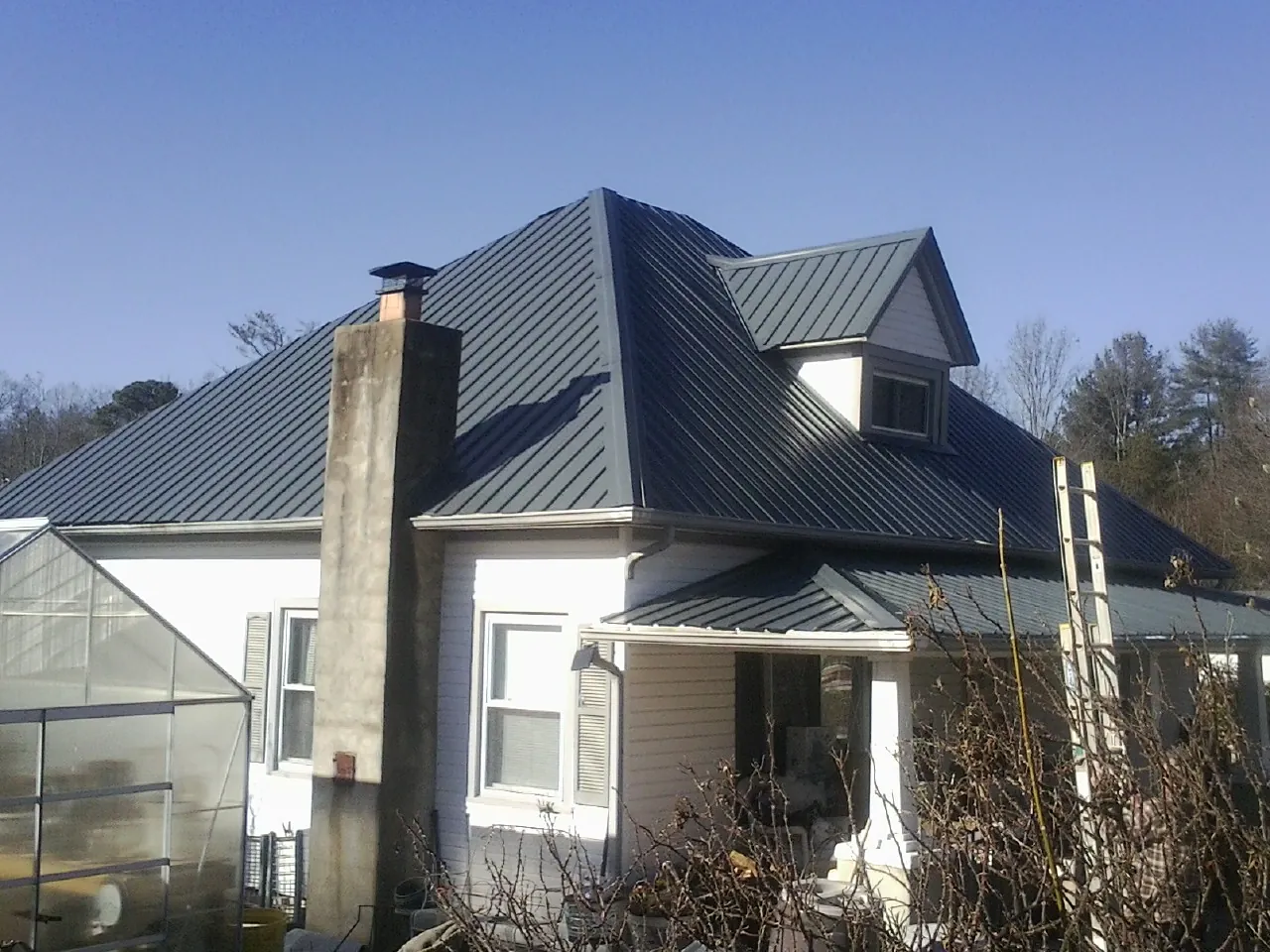 Dark blue standing seam metal roof on a white farmhouse with dormer — Slate & Tile Roof Repair by Roofing Brothers in Jackson Heights