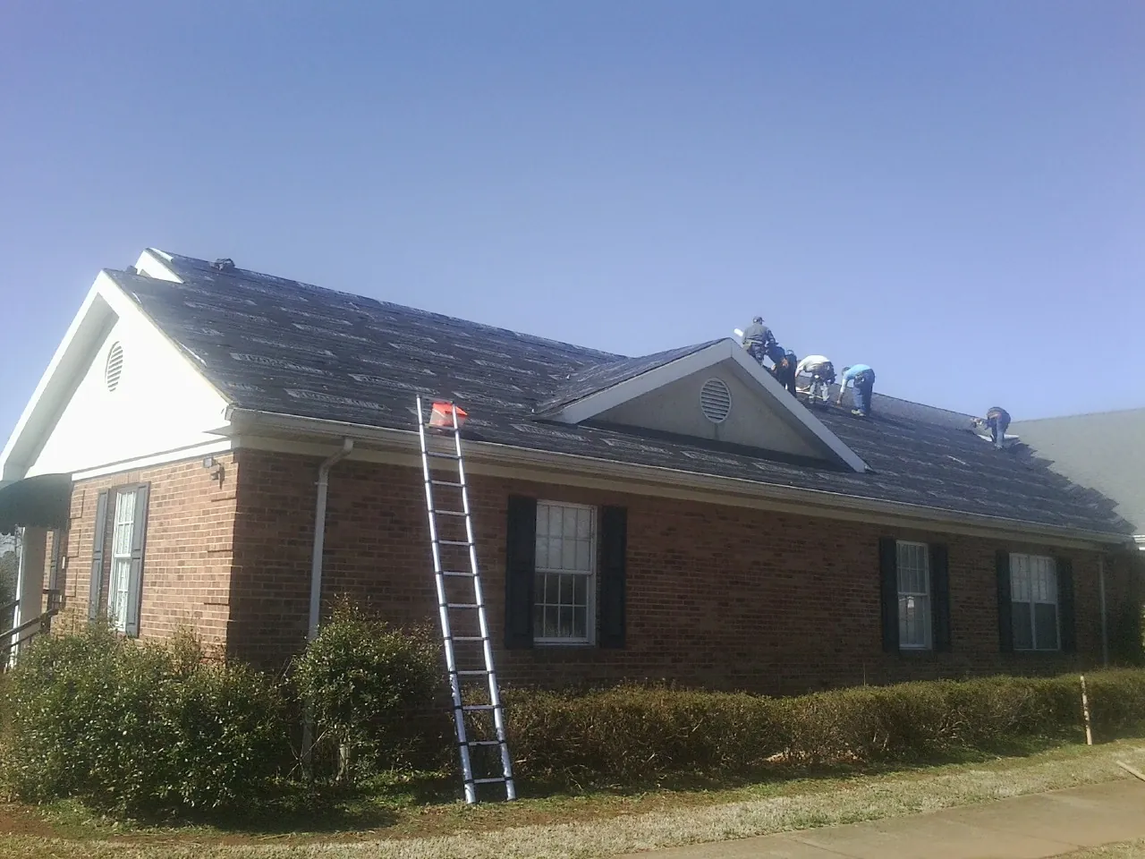 Crew tearing shingles off a brick ranch roof with a ladder set — Metal Roof Repair work by our crew in Jackson Heights