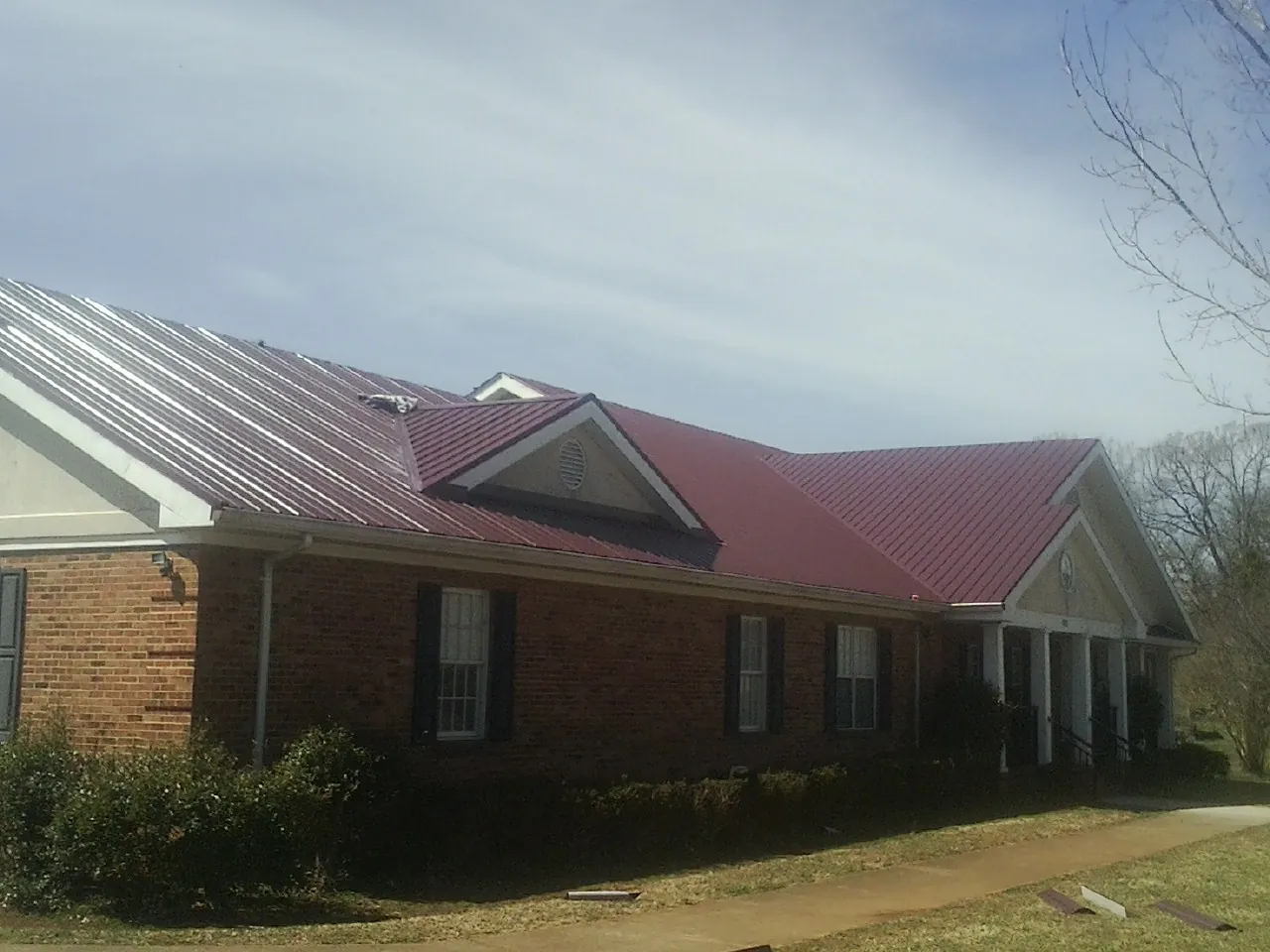 Red metal roof with gabled entries on a long brick building, from a Hail Damage Roof Repair job in Jackson Heights