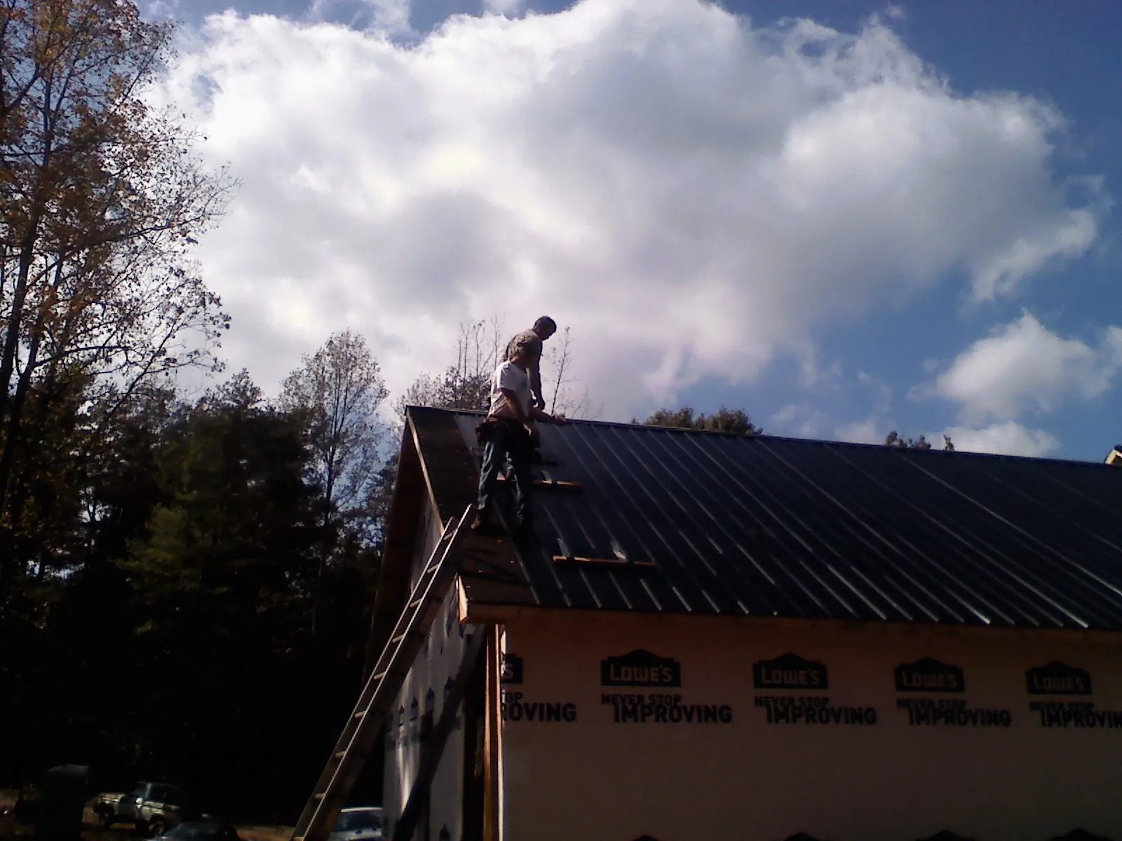 Roofer fastening dark metal panels high against a cloudy sky, from a Roof Inspection job in Jackson Heights