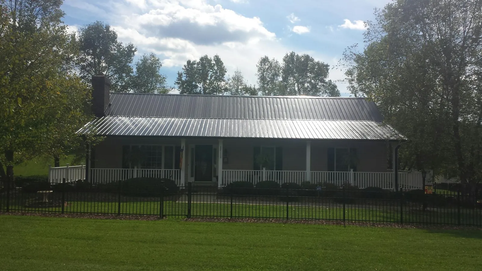 Gray metal roof on a brick ranch with a full width front porch — Gutter Guard Installation work by our crew in Jackson Heights