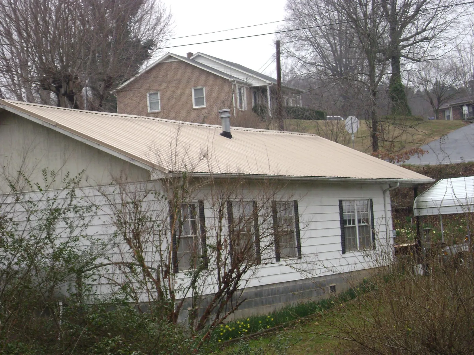 Tan metal roof on a white sided house set into a hillside — Commercial Roofing by Roofing Brothers in Jackson Heights
