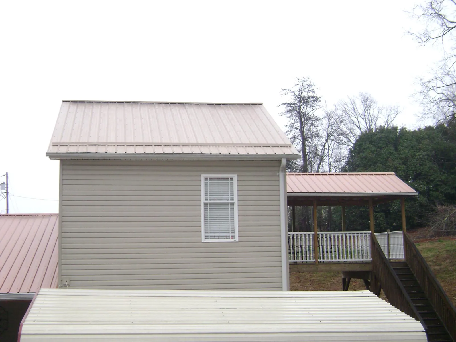 Tan metal roofs on a two story addition and attached porch, from a Roof Replacement job in Jackson Heights