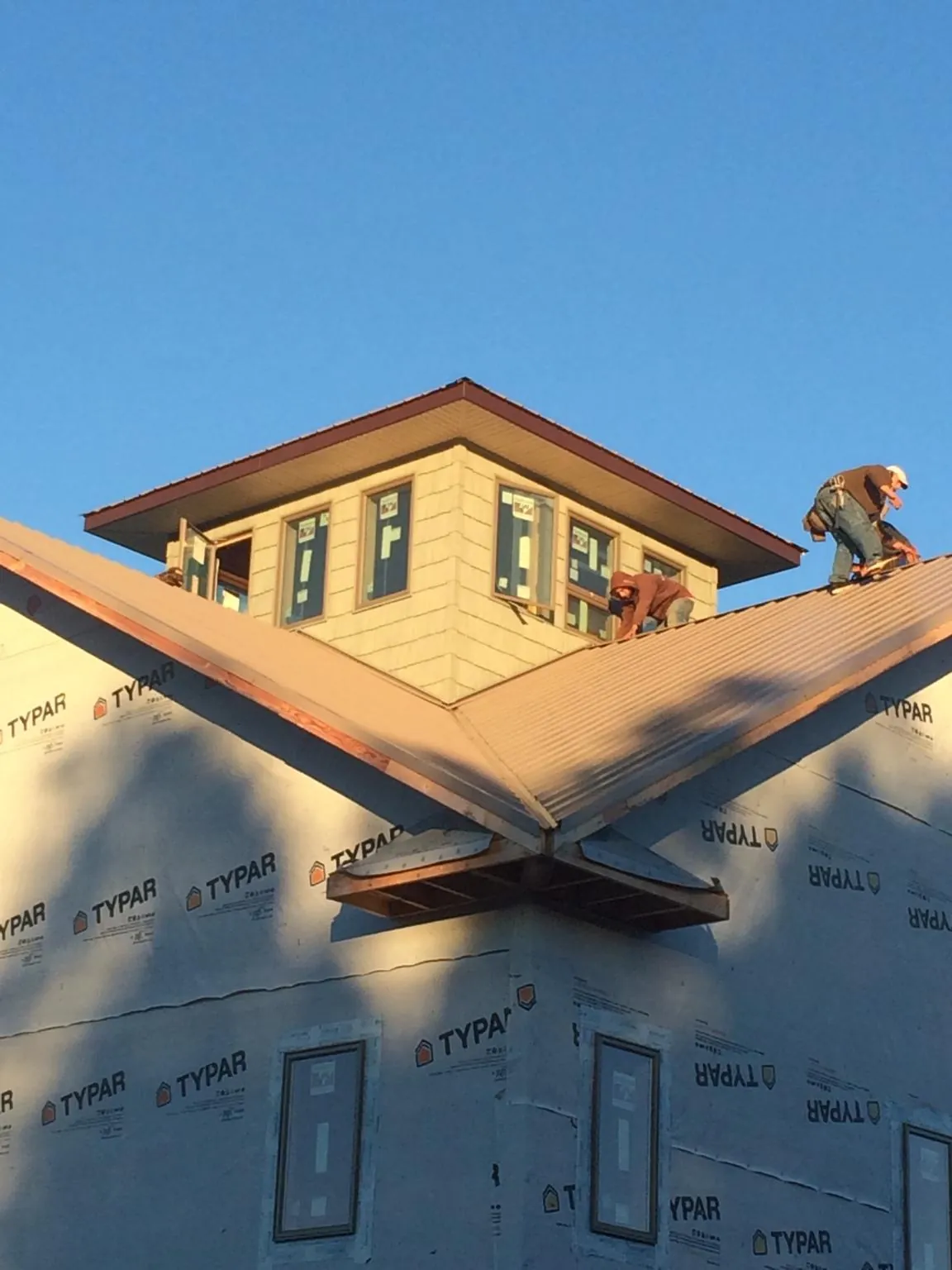 Roofers working around a rooftop cupola on a new metal roof at sunset — Roof Waterproofing in Jackson Heights by Roofing Brothers